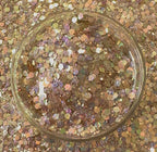 Multicolored glitter in a clear glass container on a glittery background
