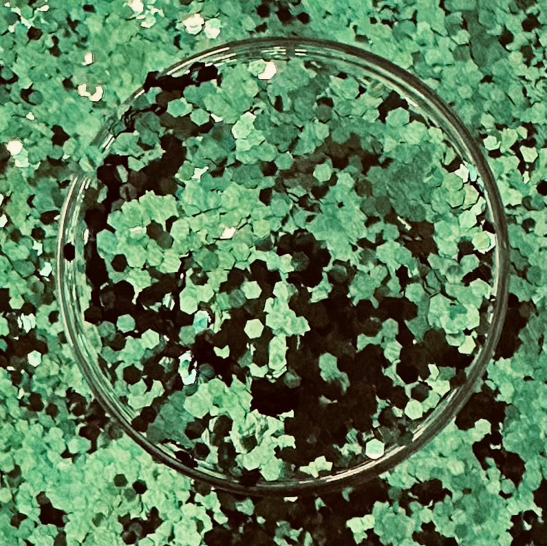 Close-up of a glass bowl filled with green chunky glitter for craft projects.